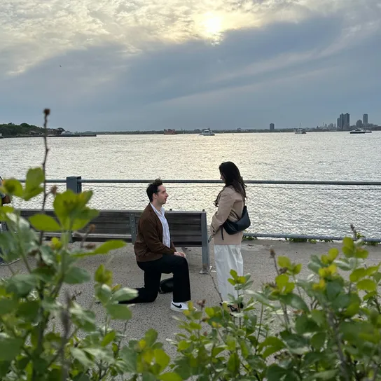 Caleb proposing on the Brooklyn bridge waterfront to Shruti, taken by a hidden photographer behind a bush (Emily).
